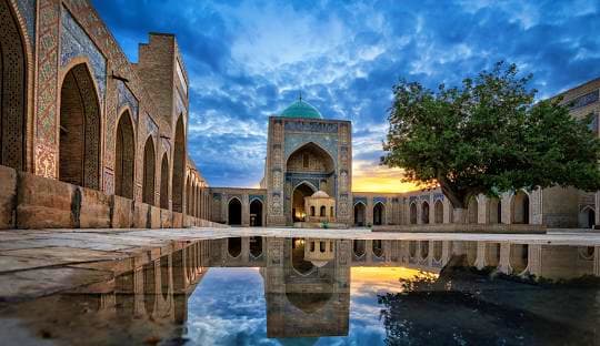 Explore Uzbekistan Al-Hakim Mosque courtyard in Isfahan, Iran, with reflecting pool and intricate Islamic architecture under dramatic blue sky a